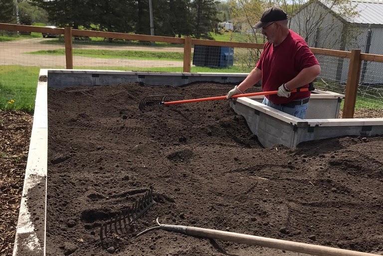 A volunteer rakes soil in our new garden beds.